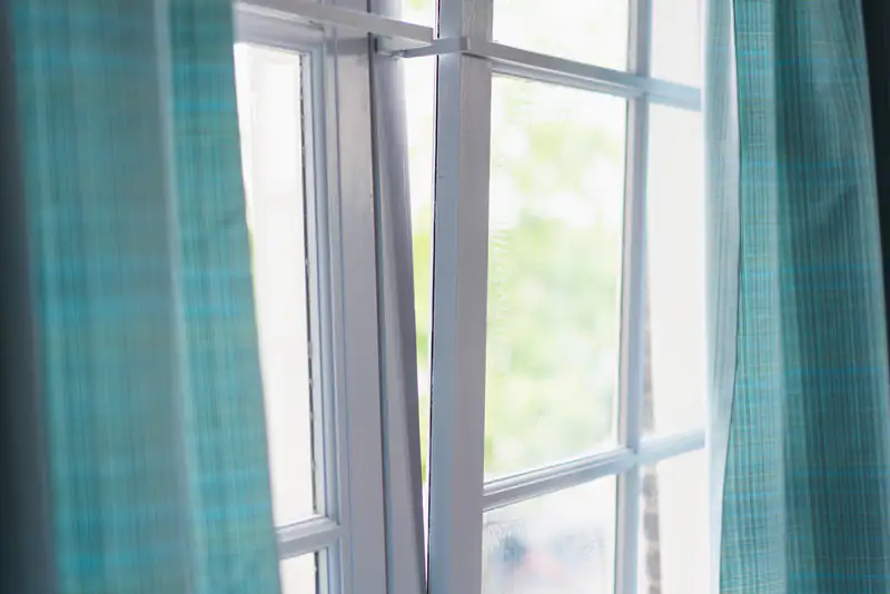 Open white double-glazed window framed by teal curtains, illustrating double glazing for homes in Newcastle upon Tyne