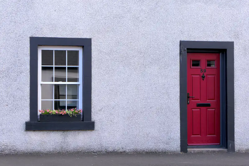 White cottage with a red front door and a small sash window, illustrating uPVC doors for homes in Heaton